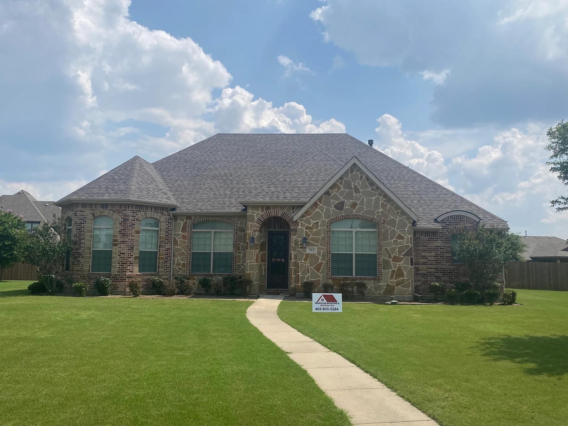 A large stone house with a gray roof and a sign in front of it.