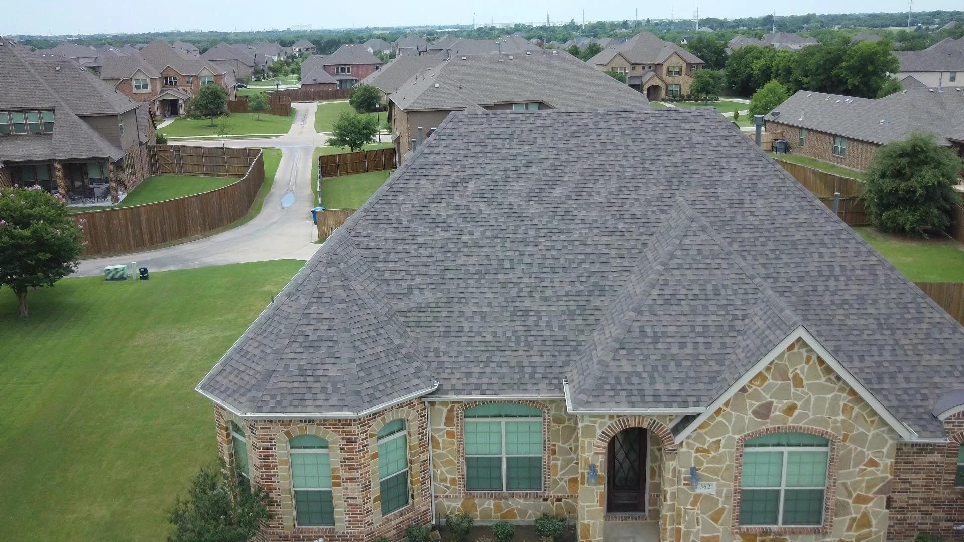 An aerial view of a brick house with a gray roof in a residential area.