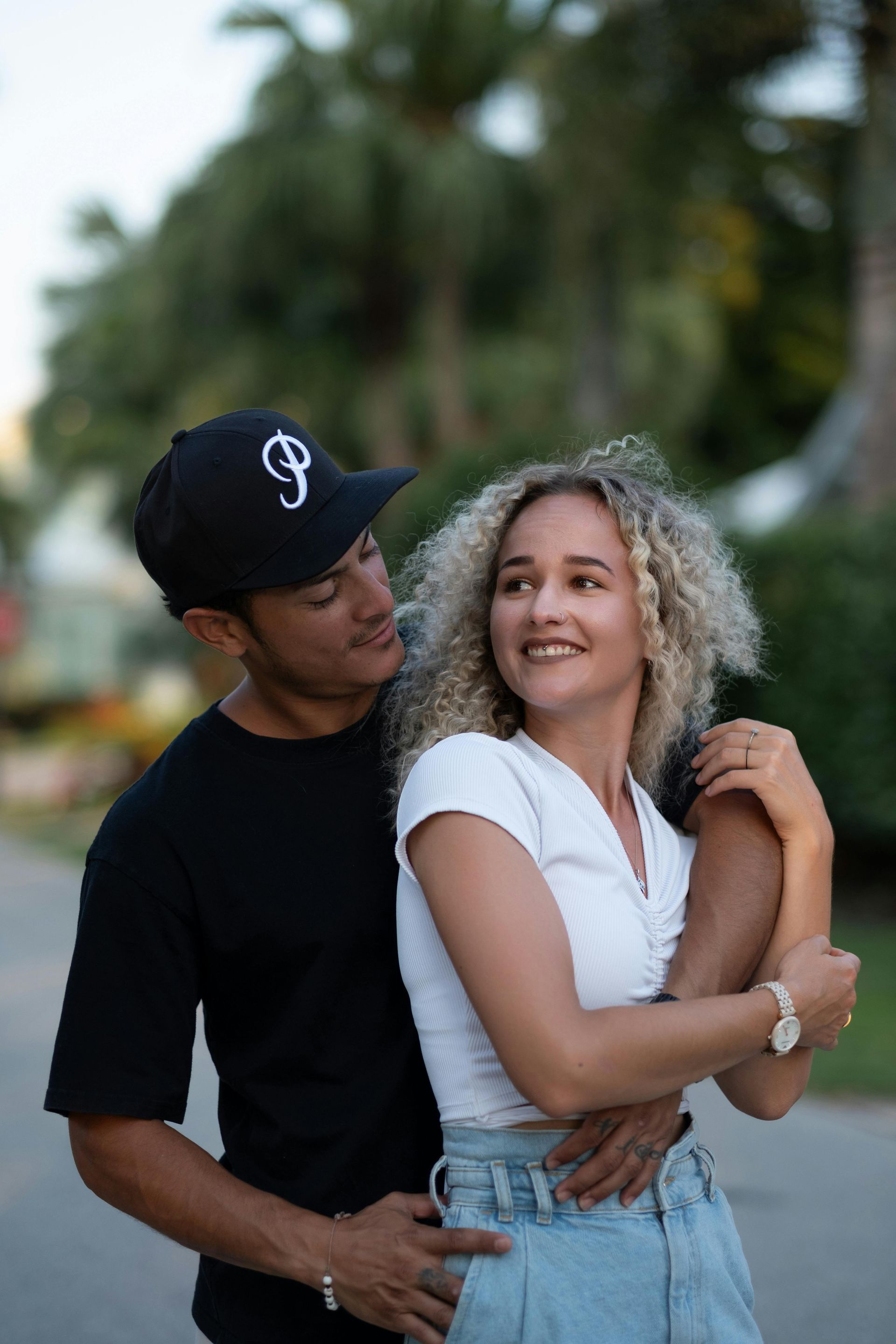 A man in a black baseball cap looking lovingly at a woman with curly blonde hair who is smiling warm