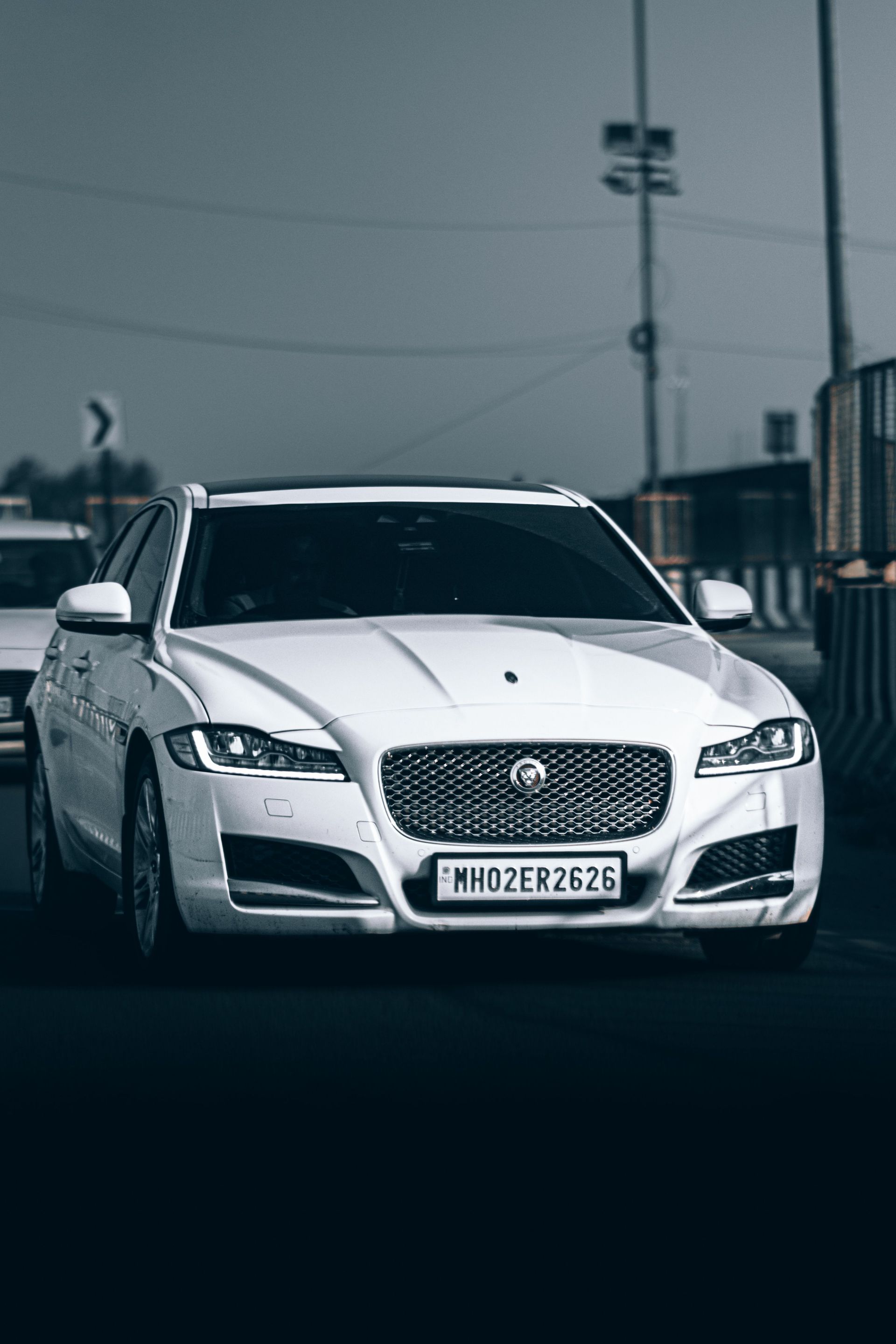 White Jaguar sedan driving on a road in a dimly lit urban setting