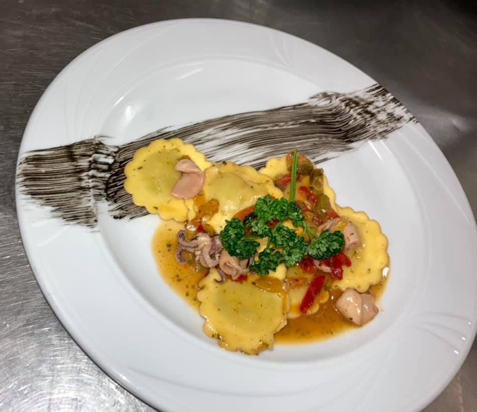 Un piatto bianco condito con ravioli e salsa