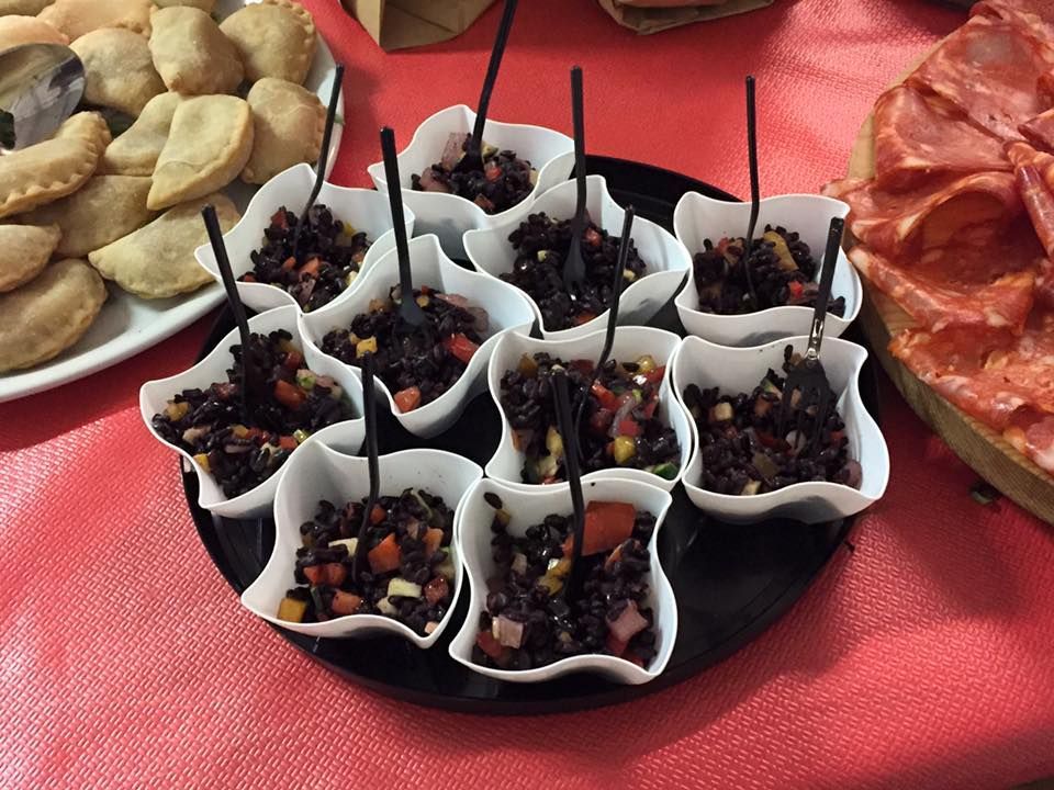 Un piatto nero sormontato da piccole ciotole di cibo con cucchiai su un tavolo.