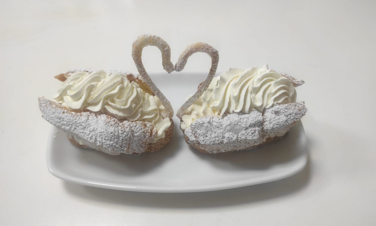 Due pasticcini a forma di cigno con panna montata su un piatto bianco.