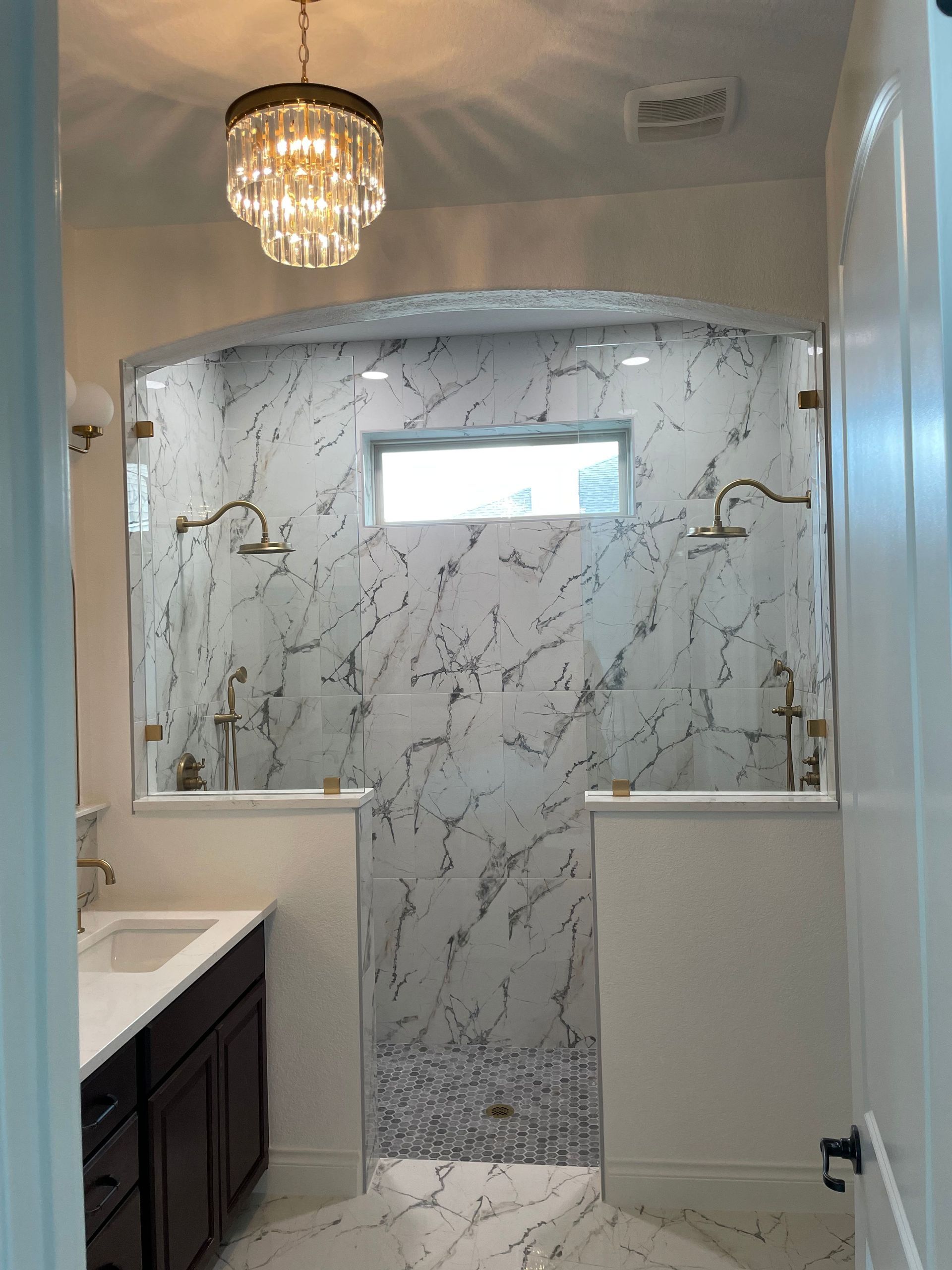 A bathroom with a sink , shower , and chandelier.