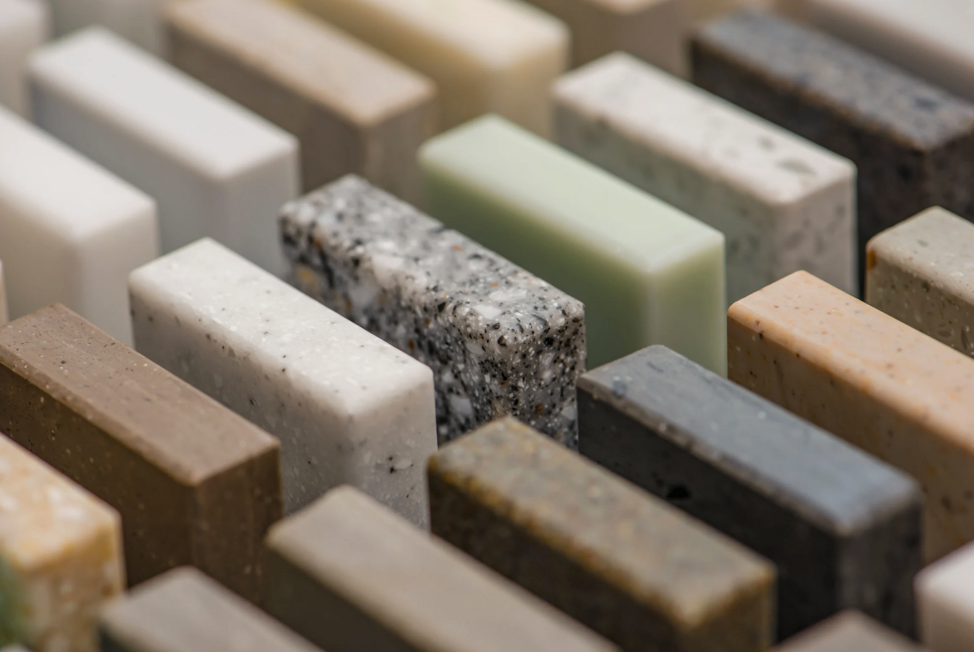 A vase filled with wooden spoons is sitting on a counter next to a marble tile wall.