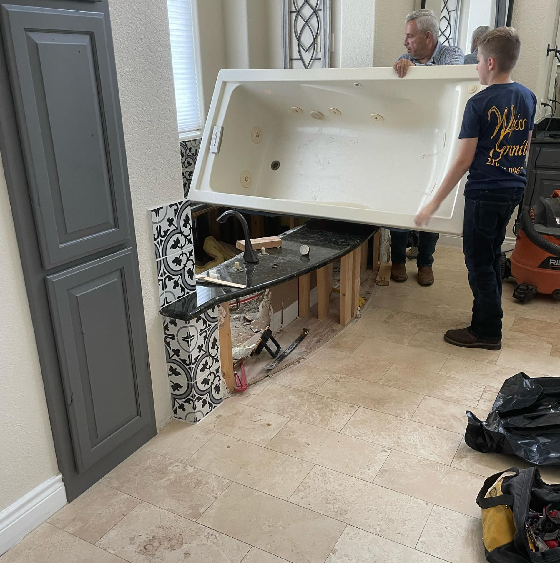 A man and a boy are carrying a bathtub in a bathroom