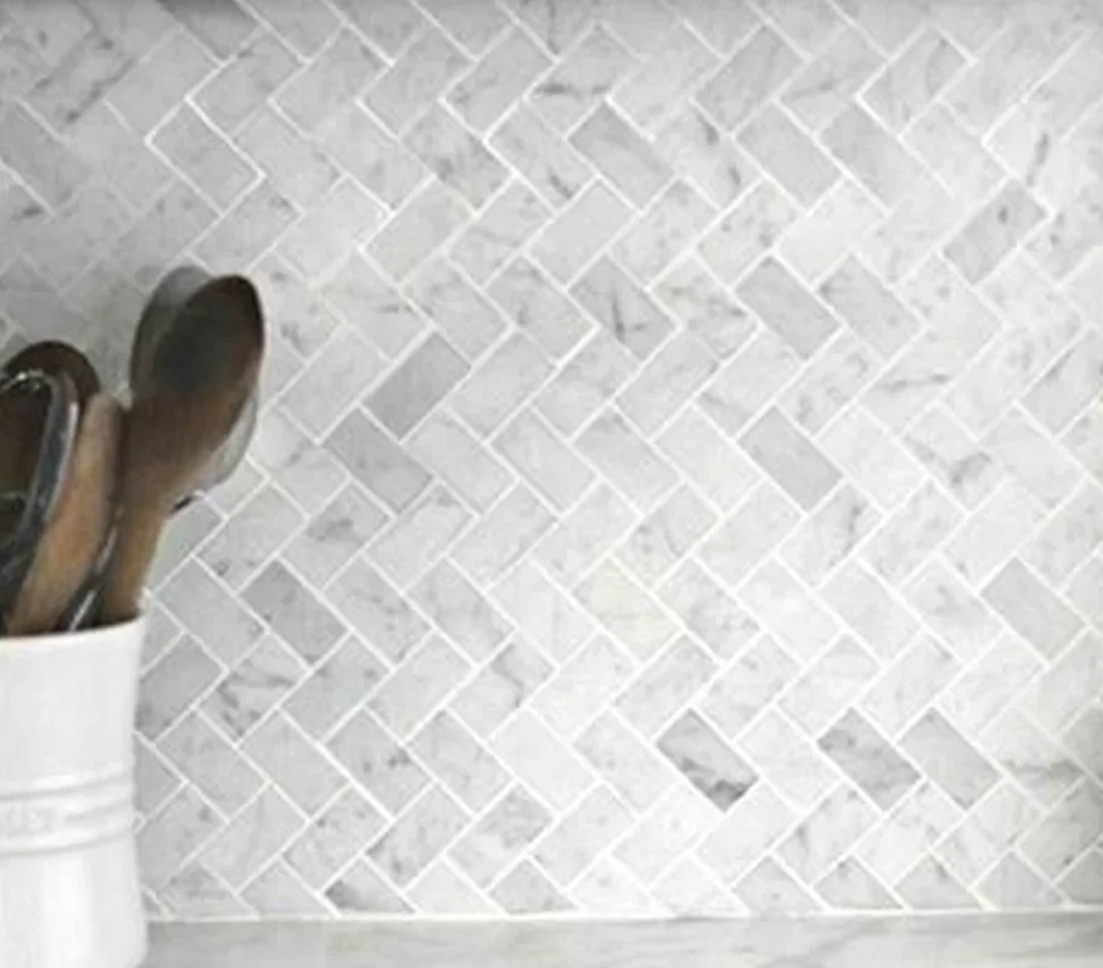A vase filled with wooden spoons is sitting on a counter next to a marble tile wall.