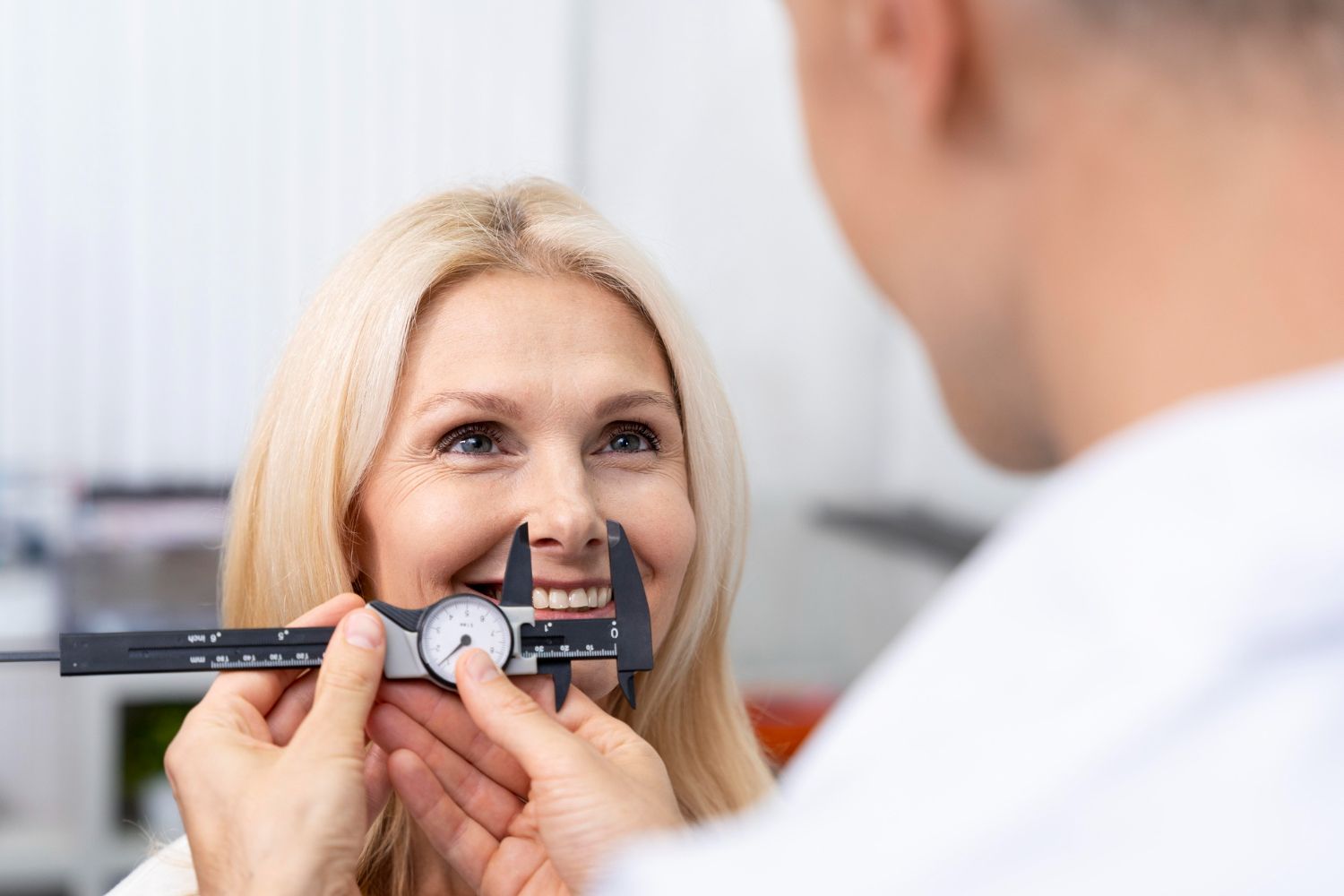 Doctor measuring woman's nose with calipers; woman smiles, inside.