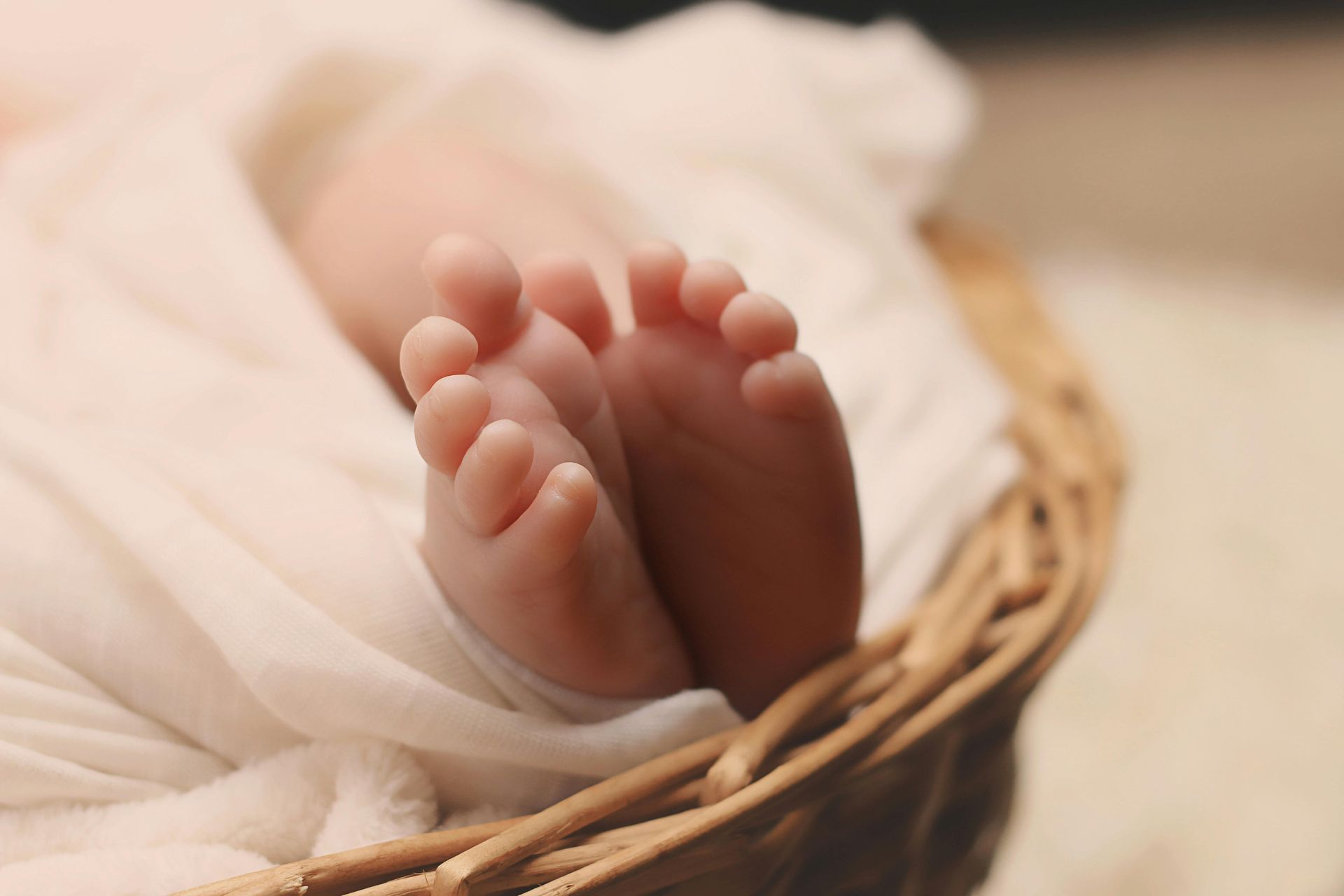 Baby's tiny feet in a wicker basket, wrapped in a white blanket.