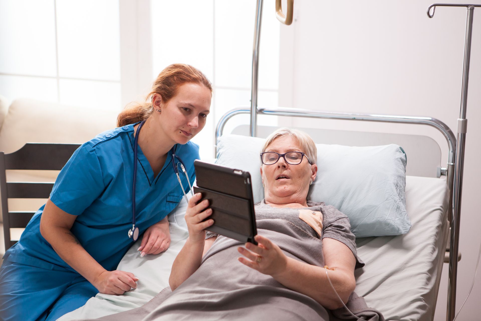 Nurse shows patient on tablet in hospital bed.