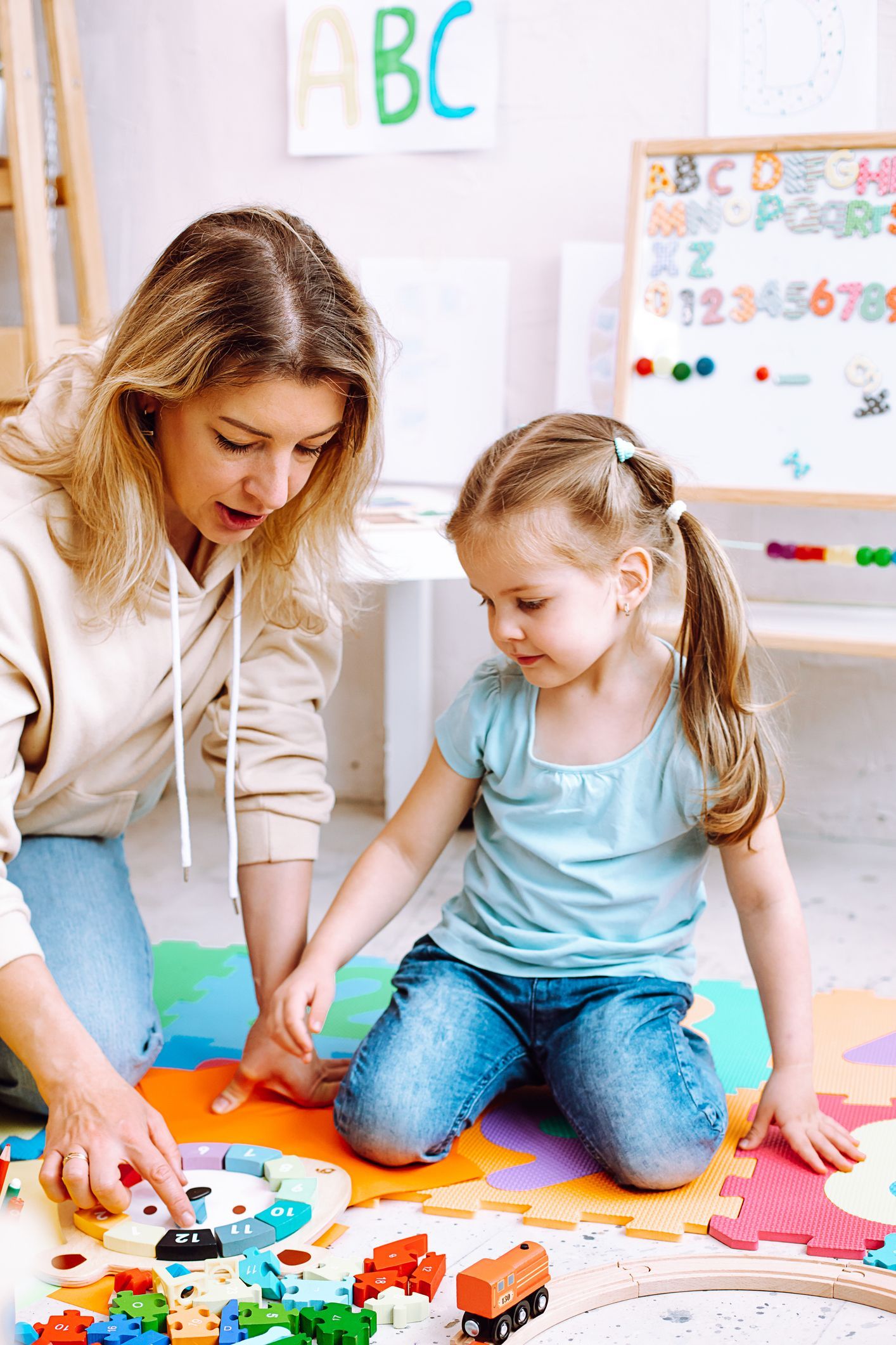 Woman and child playing on a colorful mat in a learning environment, the woman pointing at objects, the child looking down. Woman and child playing on a colorful mat in a learning environment, the woman pointing at objects, the child looking down.