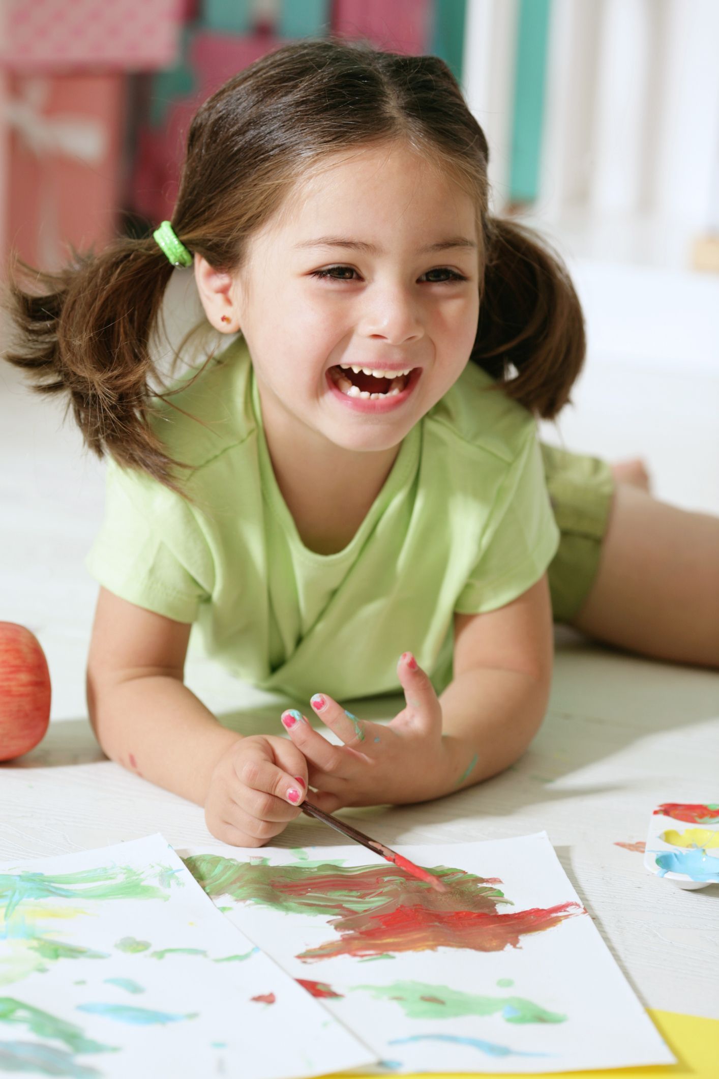Girl with brown pigtails lying on the floor, smiling and painting with watercolors. She wears a green shirt. Girl with brown pigtails lying on the floor, smiling and painting with watercolors. She wears a green shirt.