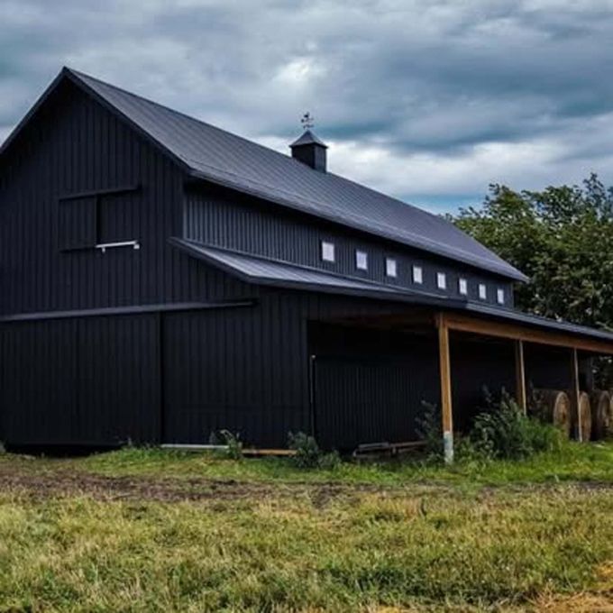 A black barn with a porch sits in the middle of a grassy field