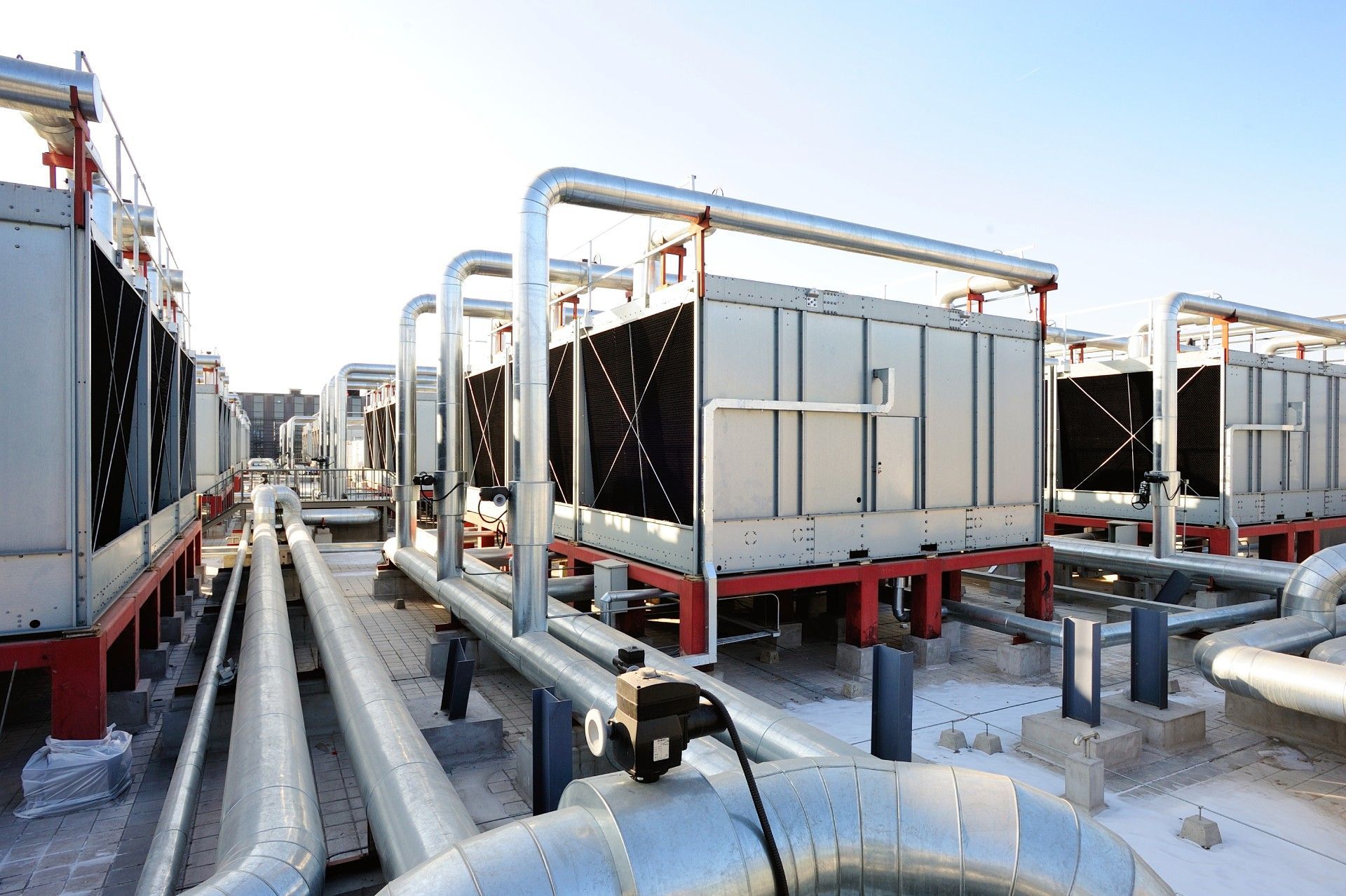 A row of cooling towers and pipes on top of a building.