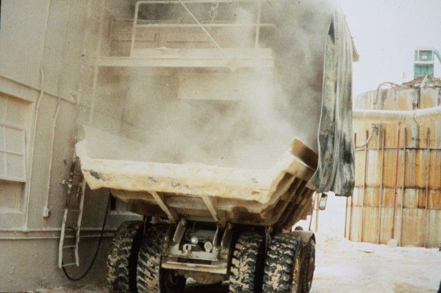 A dump truck is being loaded with sand and dust