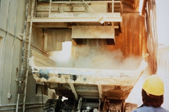 A man wearing a hard hat is standing in front of a dump truck