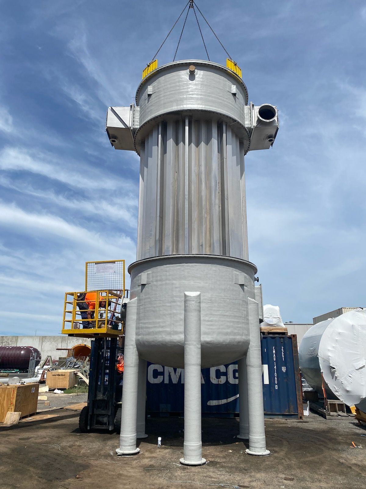 A large stainless steel tank is being lifted by a crane.