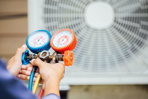 A man is holding two gauges in front of an air conditioner.