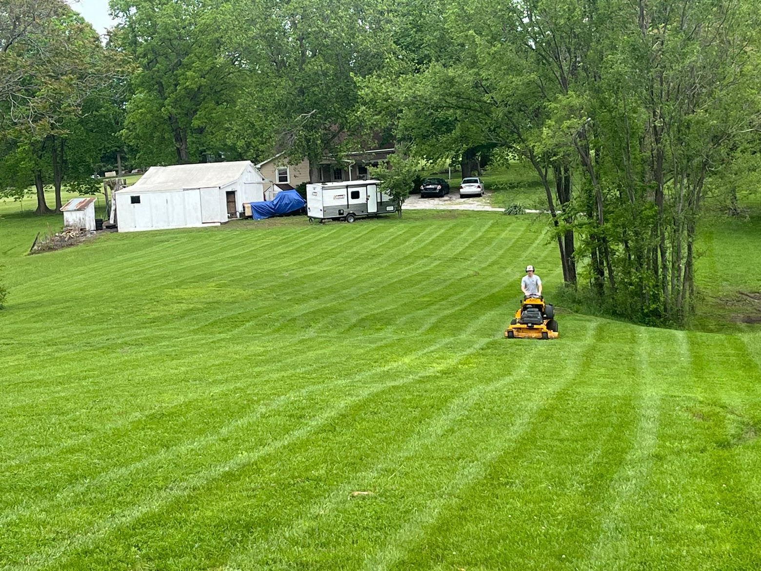 A man is riding a lawn mower through a lush green field.