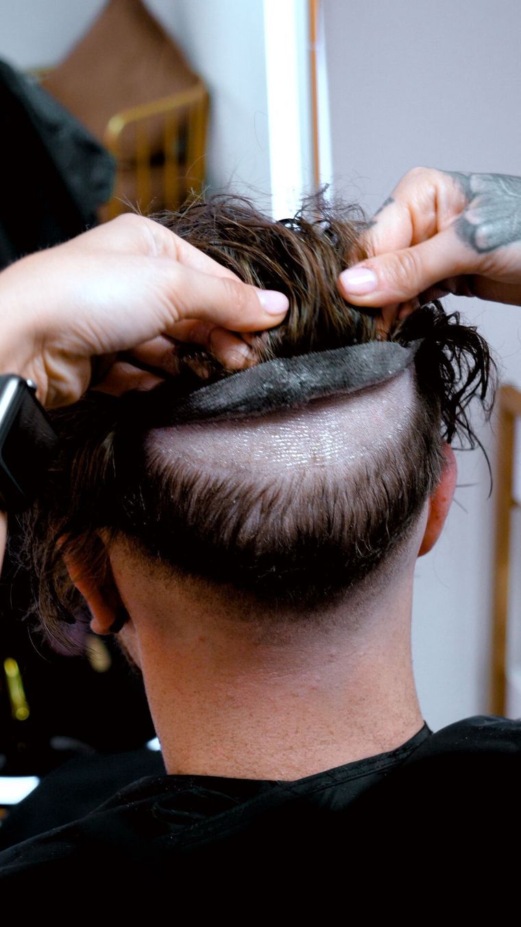 Hairdresser trims a client's hair, visible bald spot at back of head.