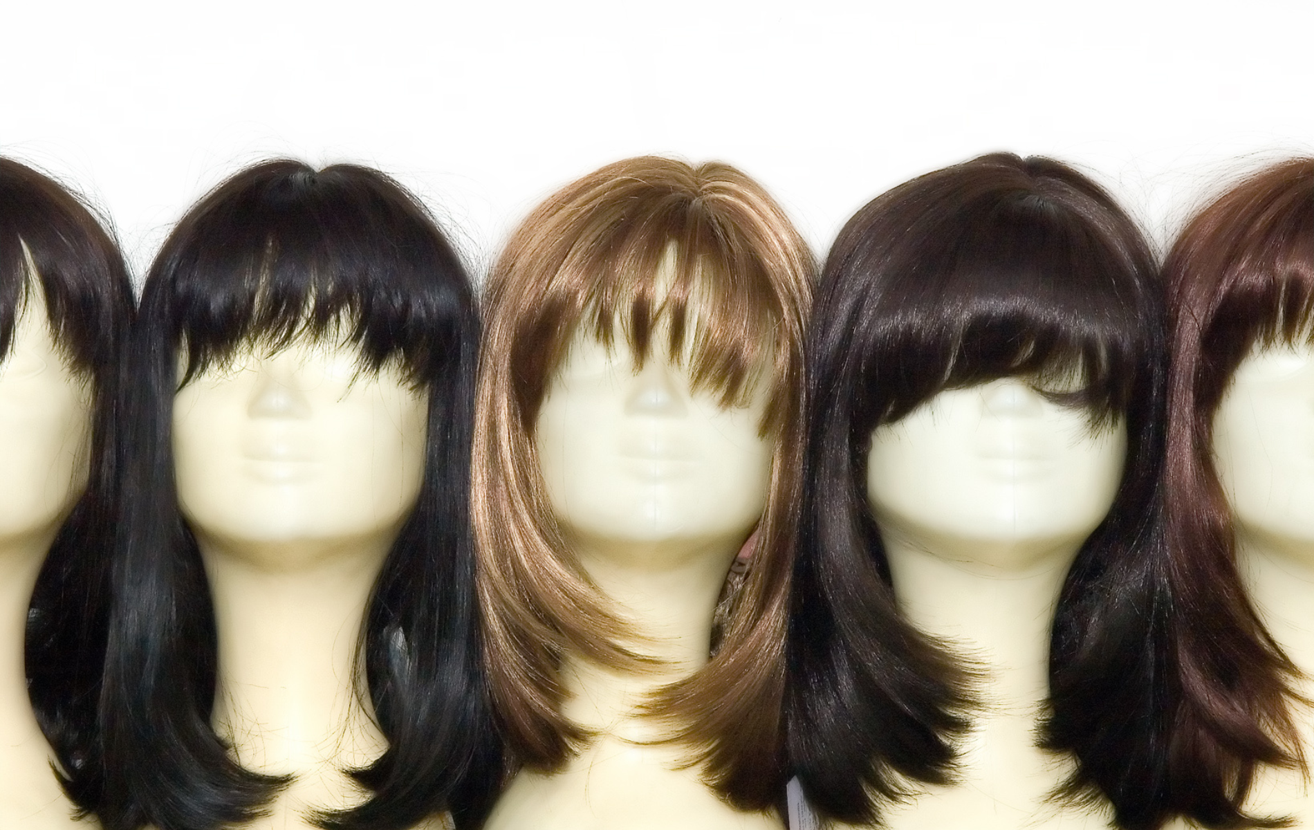 Five mannequin heads wearing various wigs, with different colors and styles.
