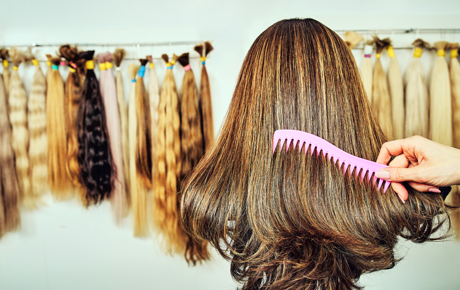 Mannequin head with brown hair being combed, surrounded by hair extensions of various colors.