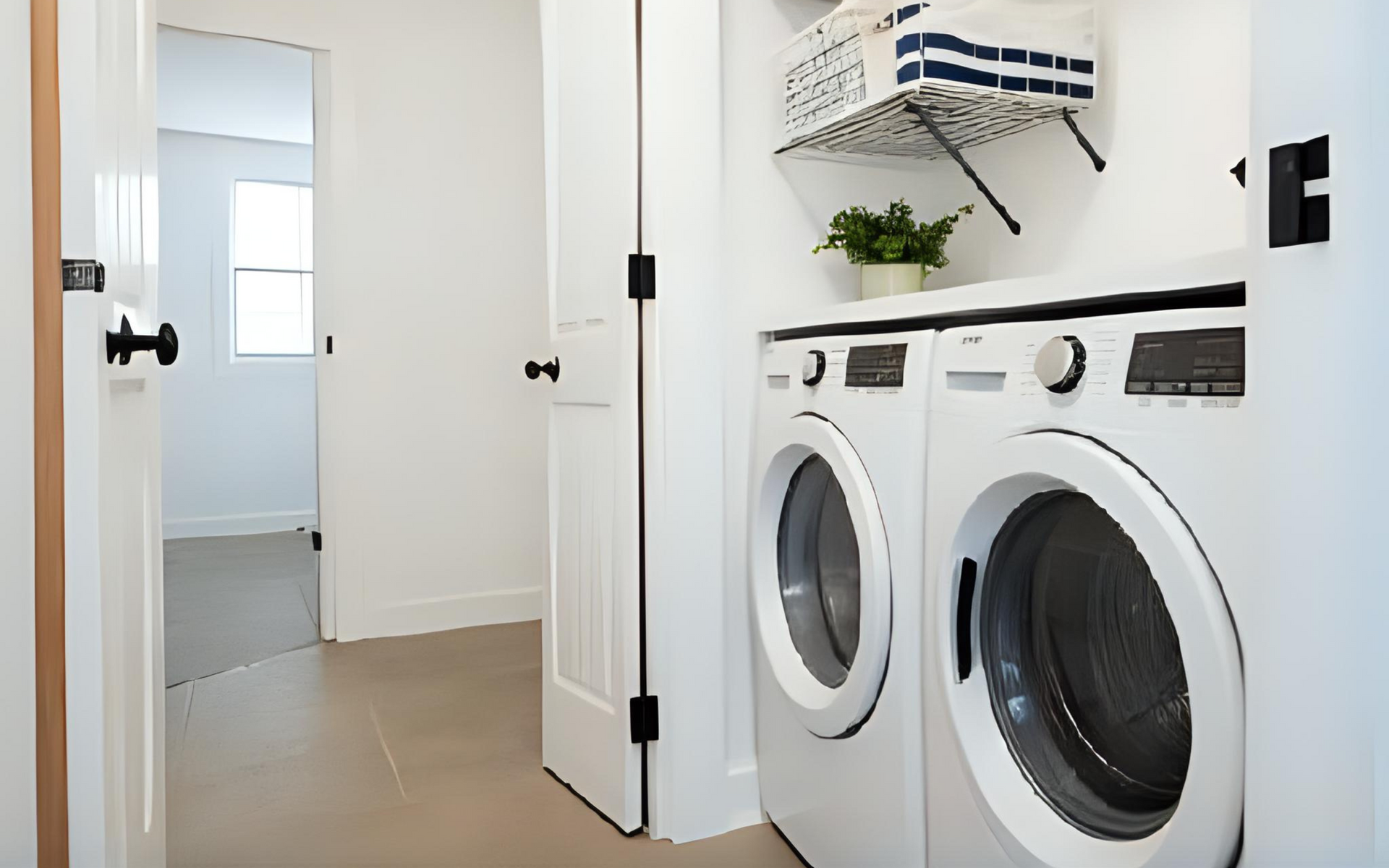 Laundry room with white washer and dryer, open door, and shelf with plant and basket.