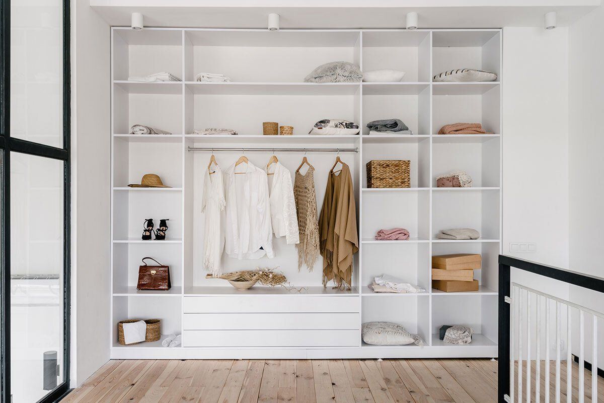 White built-in closet with shelves, drawers, and hanging clothes in a modern, well-lit space.