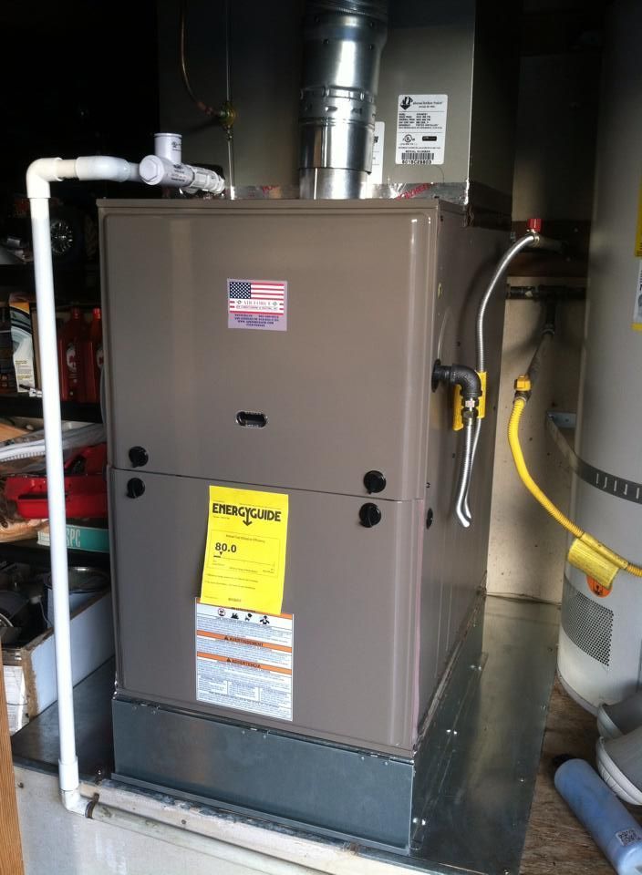 A brown furnace with ductwork and a water heater in a utility room.