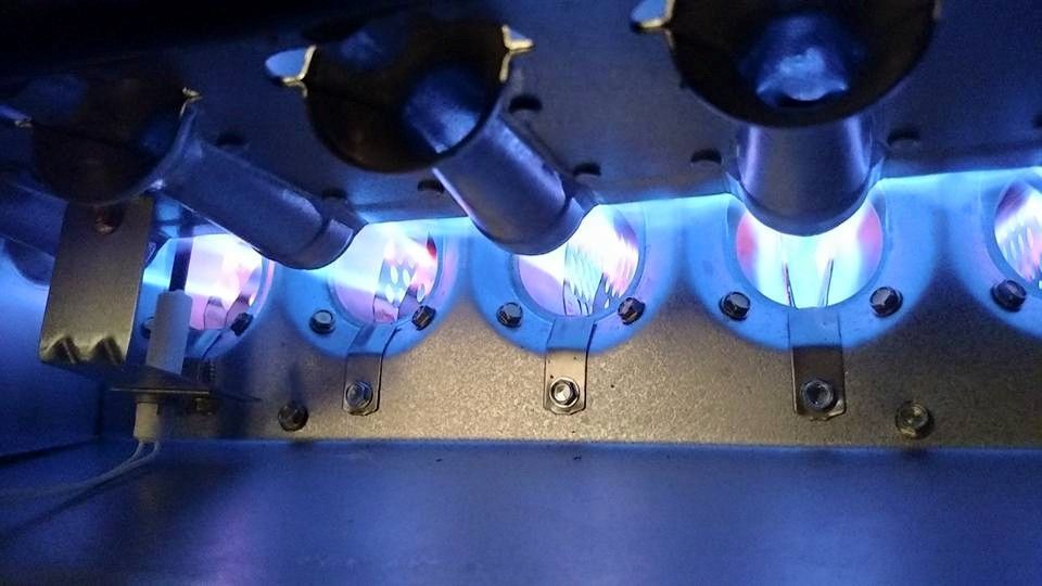 Blue flames burning inside a furnace, visible through round openings.