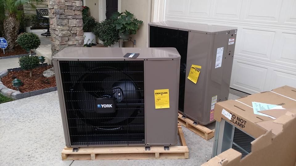 Two new air conditioning units on pallets sit outside a house.