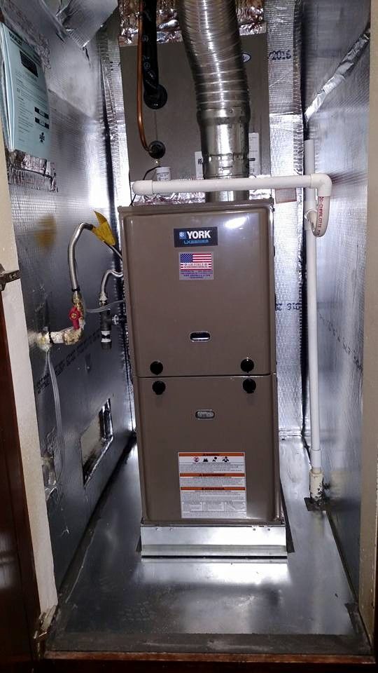 Furnace unit inside a metal enclosure. Brown unit with silver ductwork and pipes.