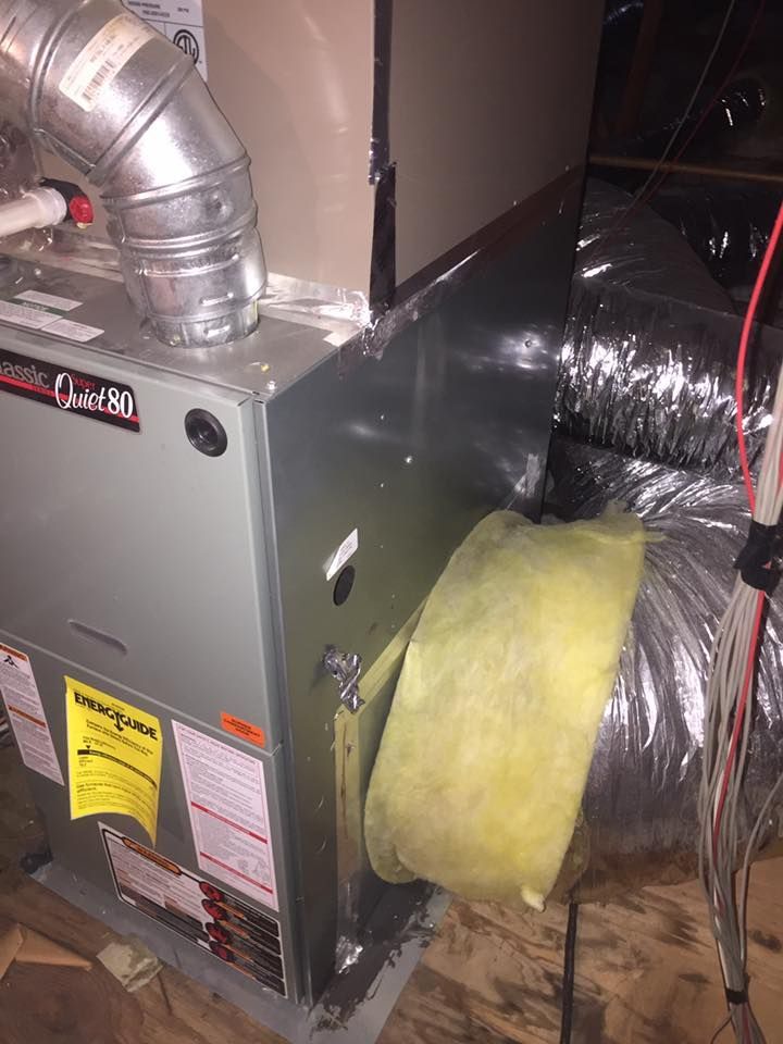 Furnace with silver ductwork and yellow insulation in an enclosed space.