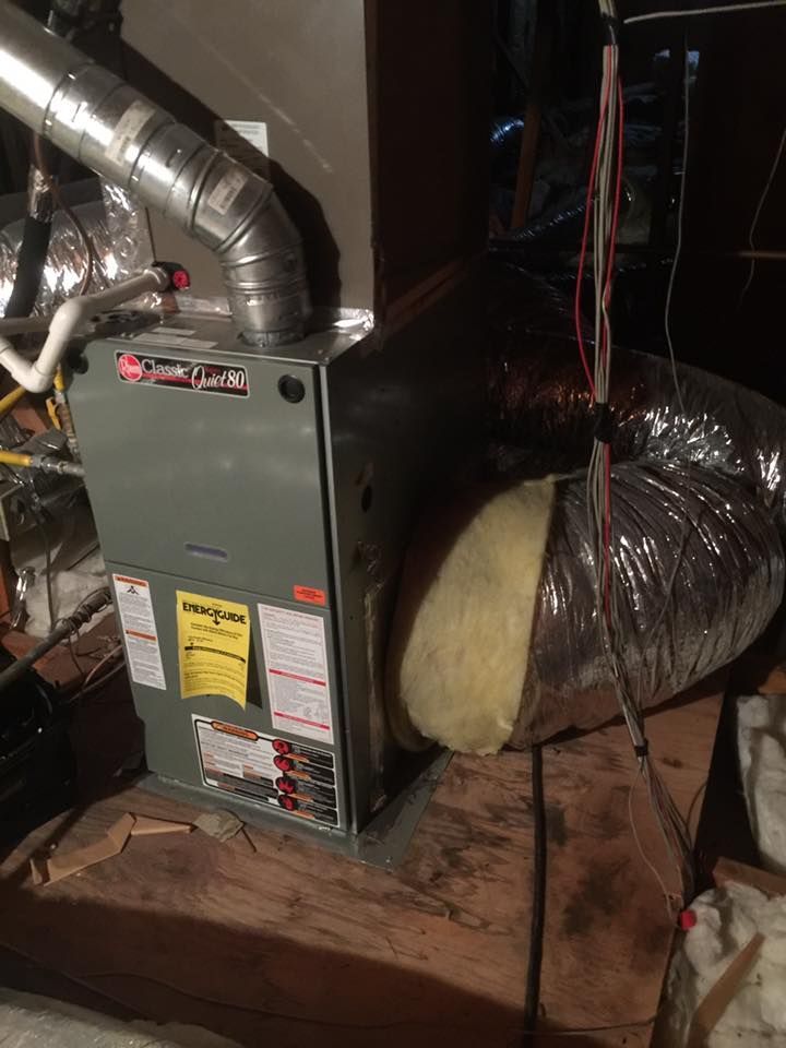 A furnace unit in a basement setting with ductwork. Grey exterior with a yellow energy sticker.