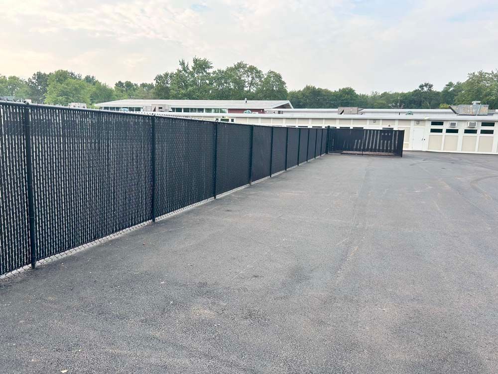 A black chain link fence surrounds a parking lot in front of a building.