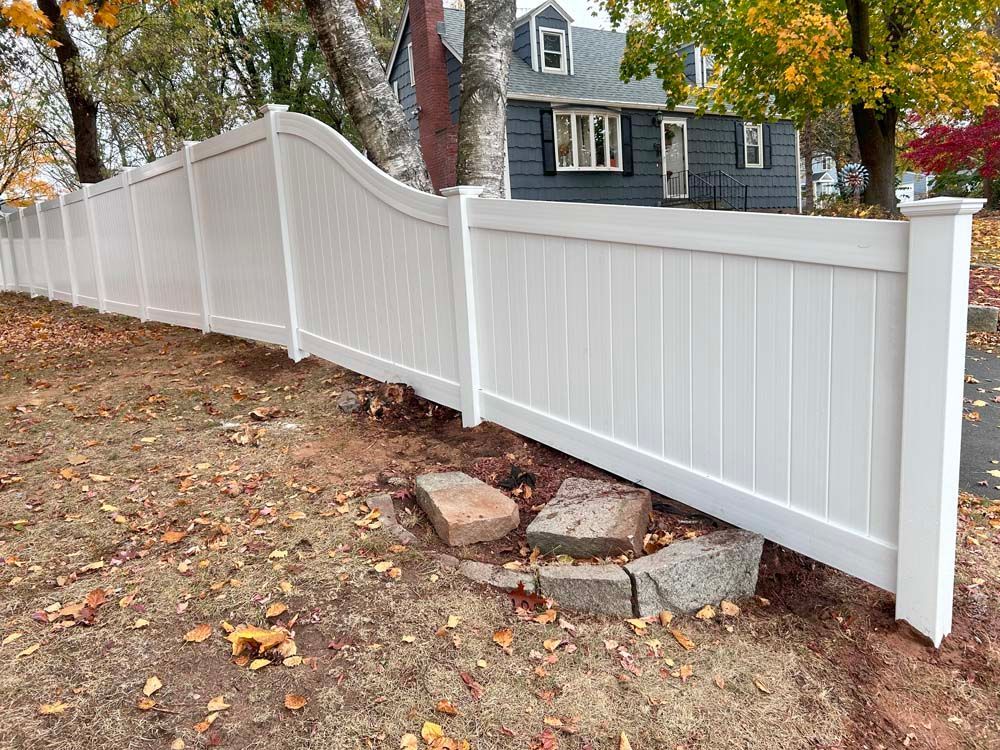A white vinyl fence surrounds a yard in front of a house.