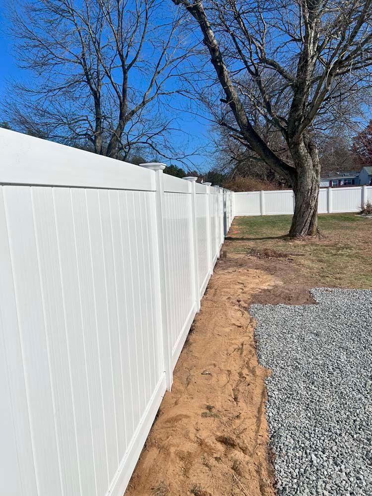 A white vinyl fence is surrounding a gravel driveway.