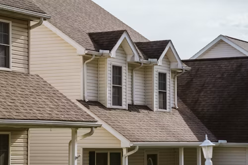 Tan house roofs with dormer windows and white trim on a suburban home