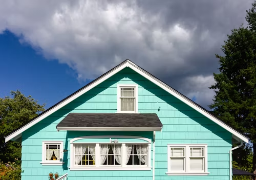 A blue house with white trim and a black roof on a cloudy day.