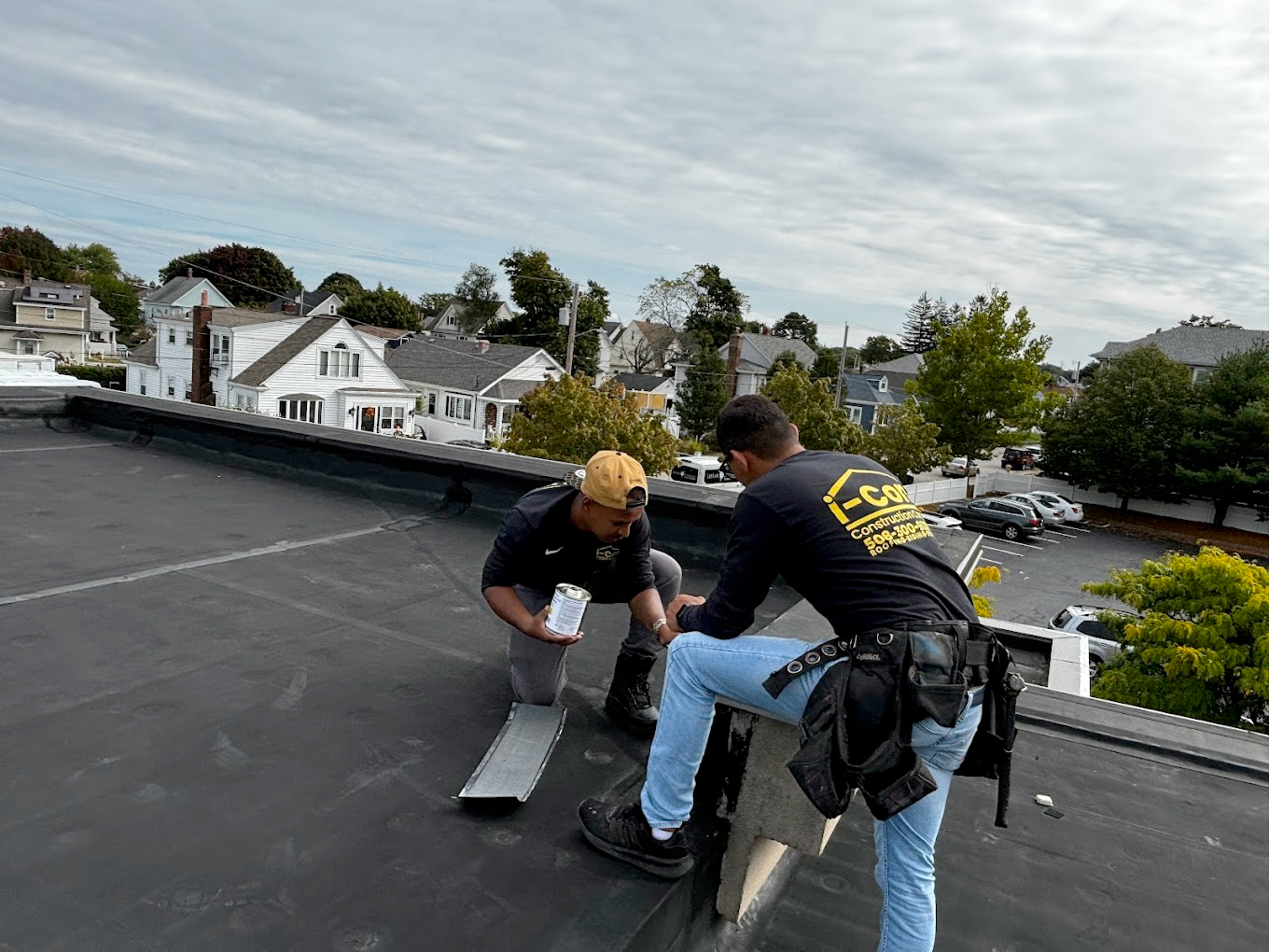 Two workers installing roofing on a flat roof, city buildings in the background.