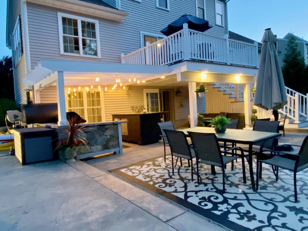 Backyard patio with dining set, outdoor kitchen, and upper deck. String lights illuminate the space.