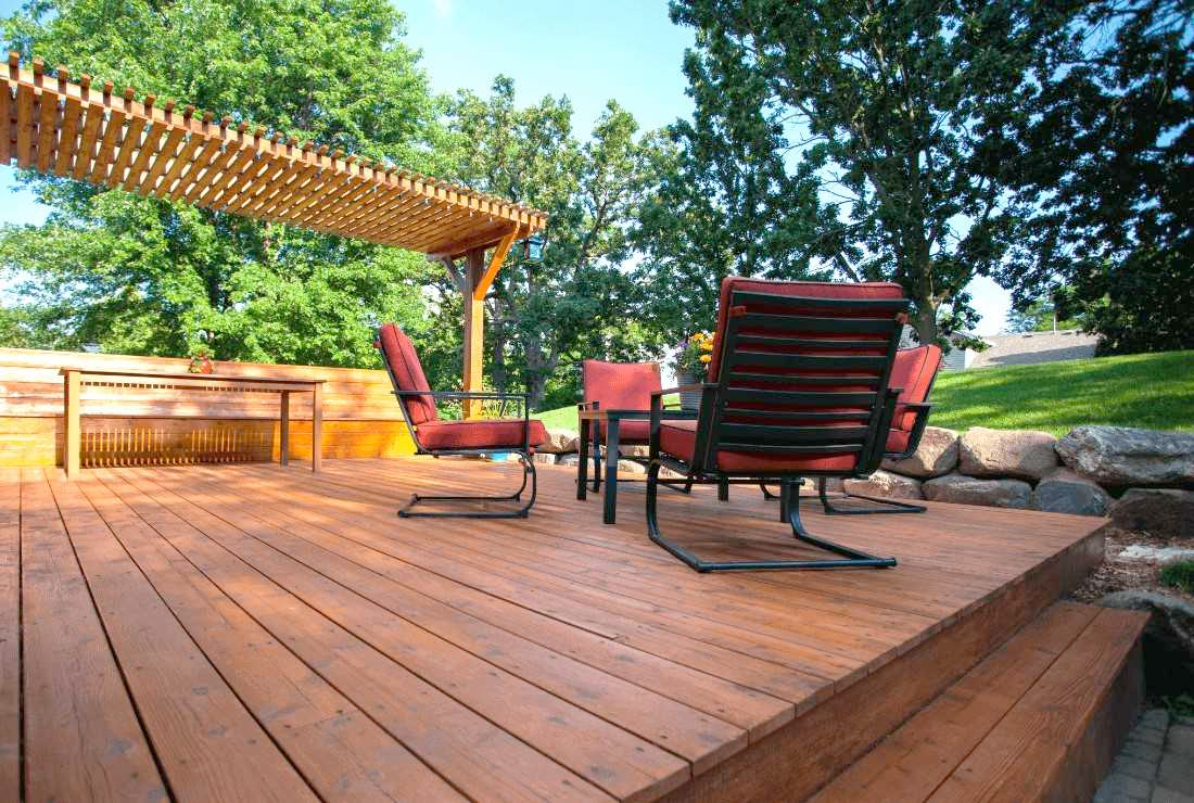 Wooden deck with red chairs, pergola, and green trees in a backyard.