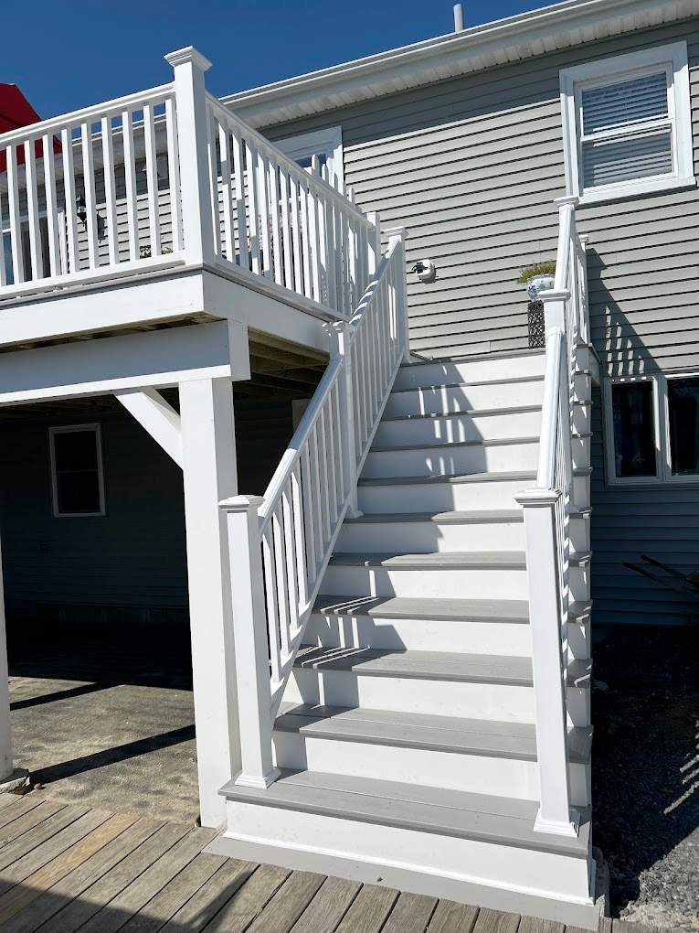 Outdoor staircase with white railing and gray steps leading to a raised deck.