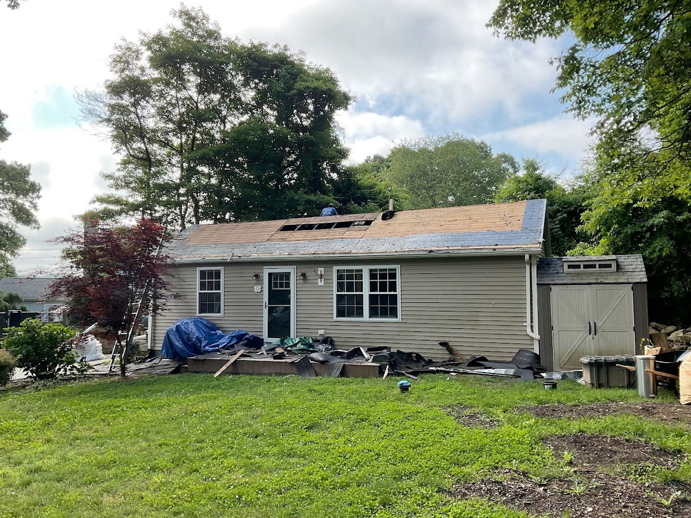 Damaged house exterior after a storm, with roof damage and debris in the yard.