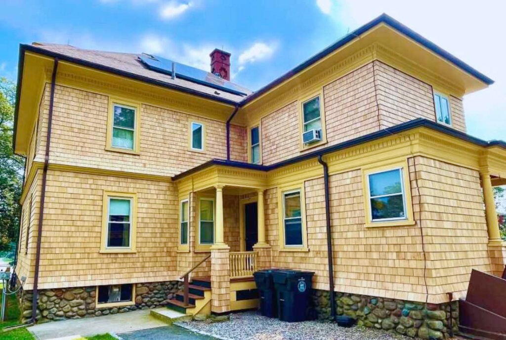 Yellow shingled house with stone foundation, solar panels, and a red chimney.