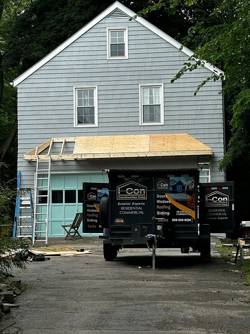 House under construction with a trailer in front. Blue siding, partially open garage, and a ladder.