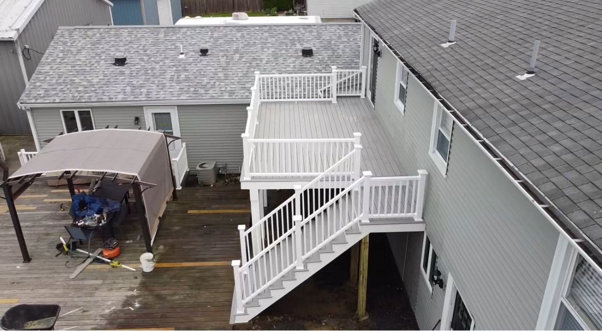 Aerial view of a white deck with stairs attached to a gray house, shed in the background, canopy in the foreground.