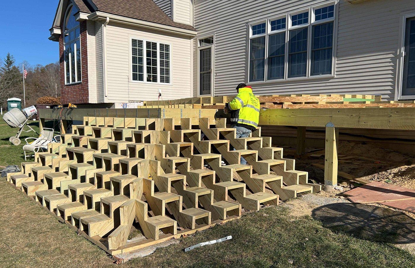 Construction worker building deck steps on a house, made of wooden blocks, sunny day.