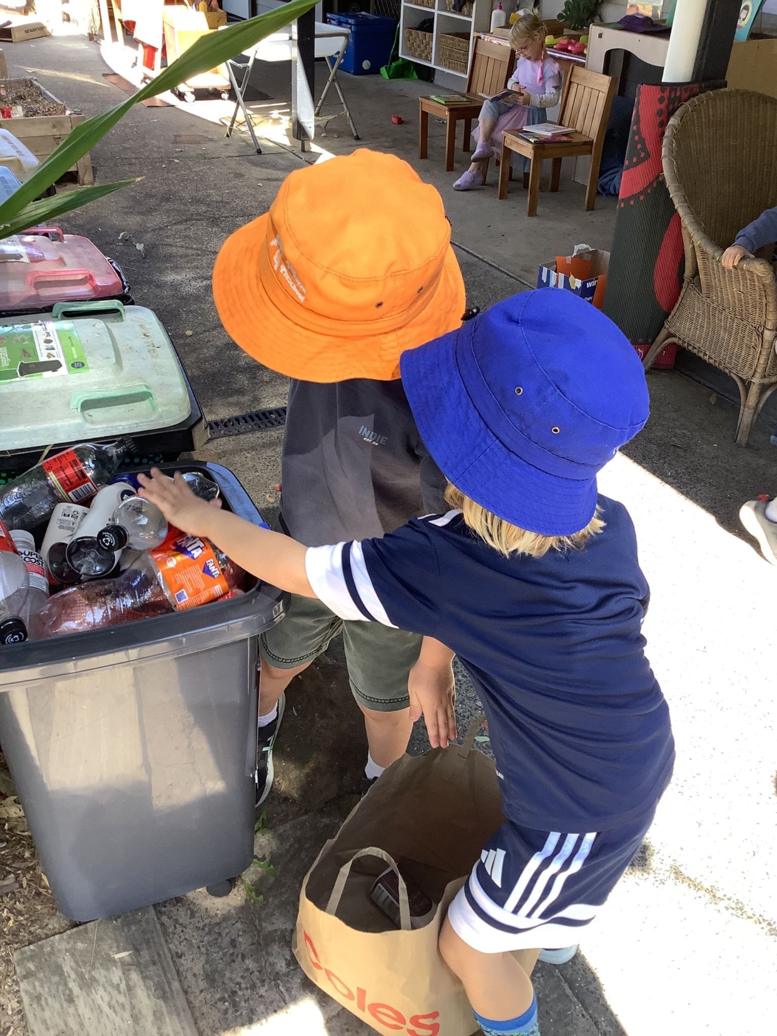 Two children in hats sort through a recycling bin outdoors - Kinburra Preschool (Kincumber) in Kincumber, NSW