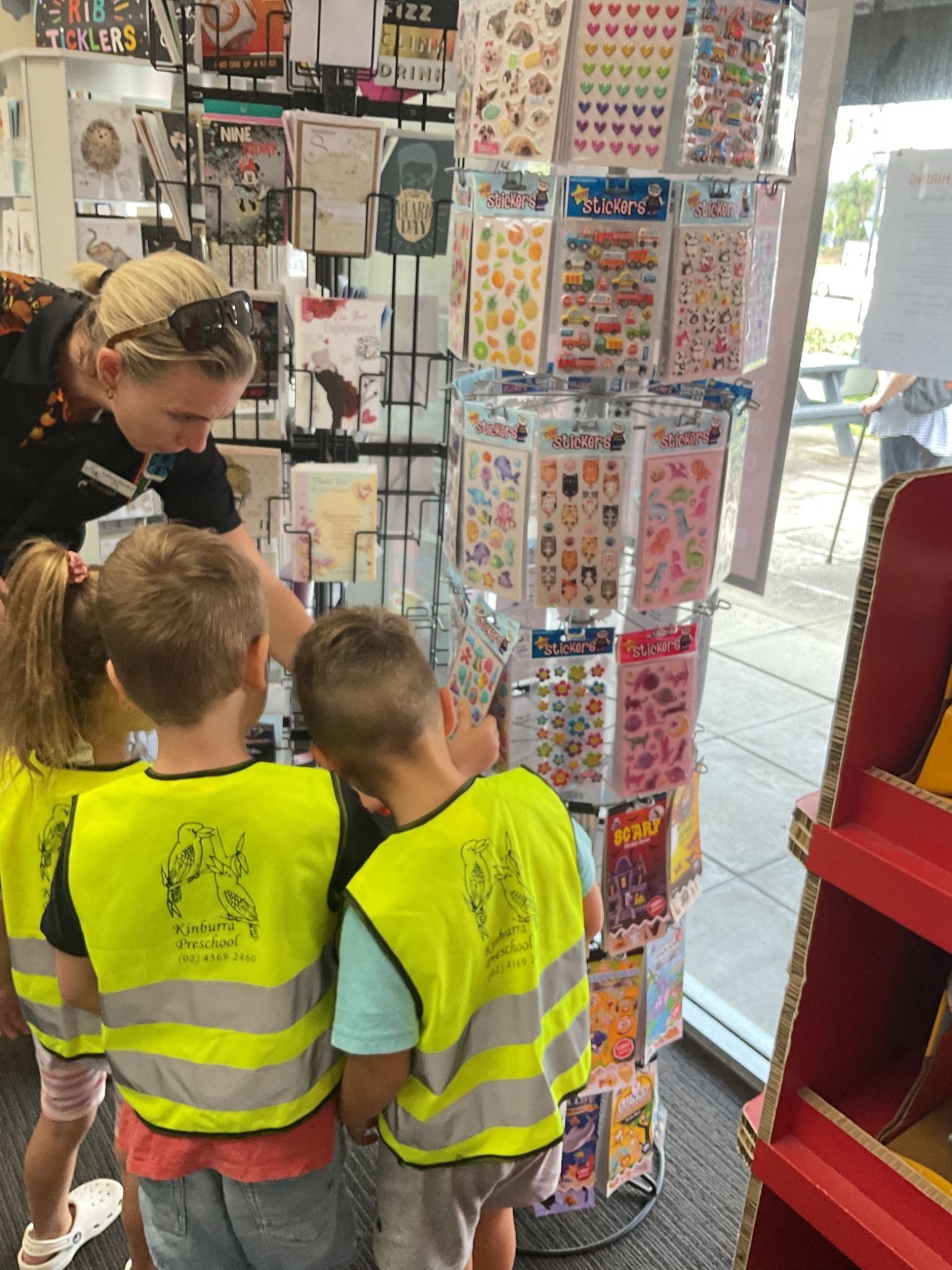 Children in yellow vests and an adult browse stickers in a store. — Kinburra Preschool (Kincumber) in Kincumber, NSW